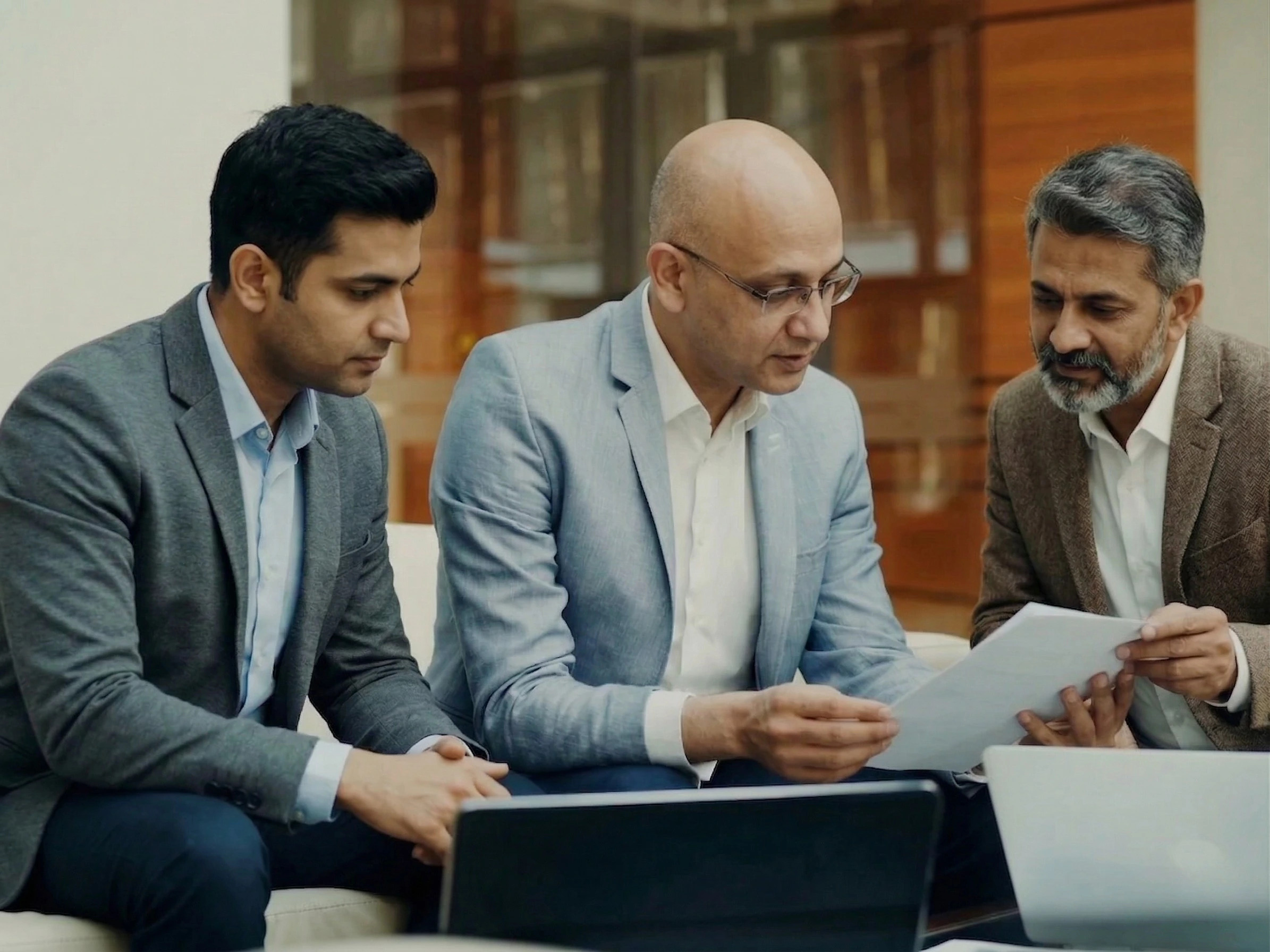 Three business professionals reviewing documents together in a modern office lounge